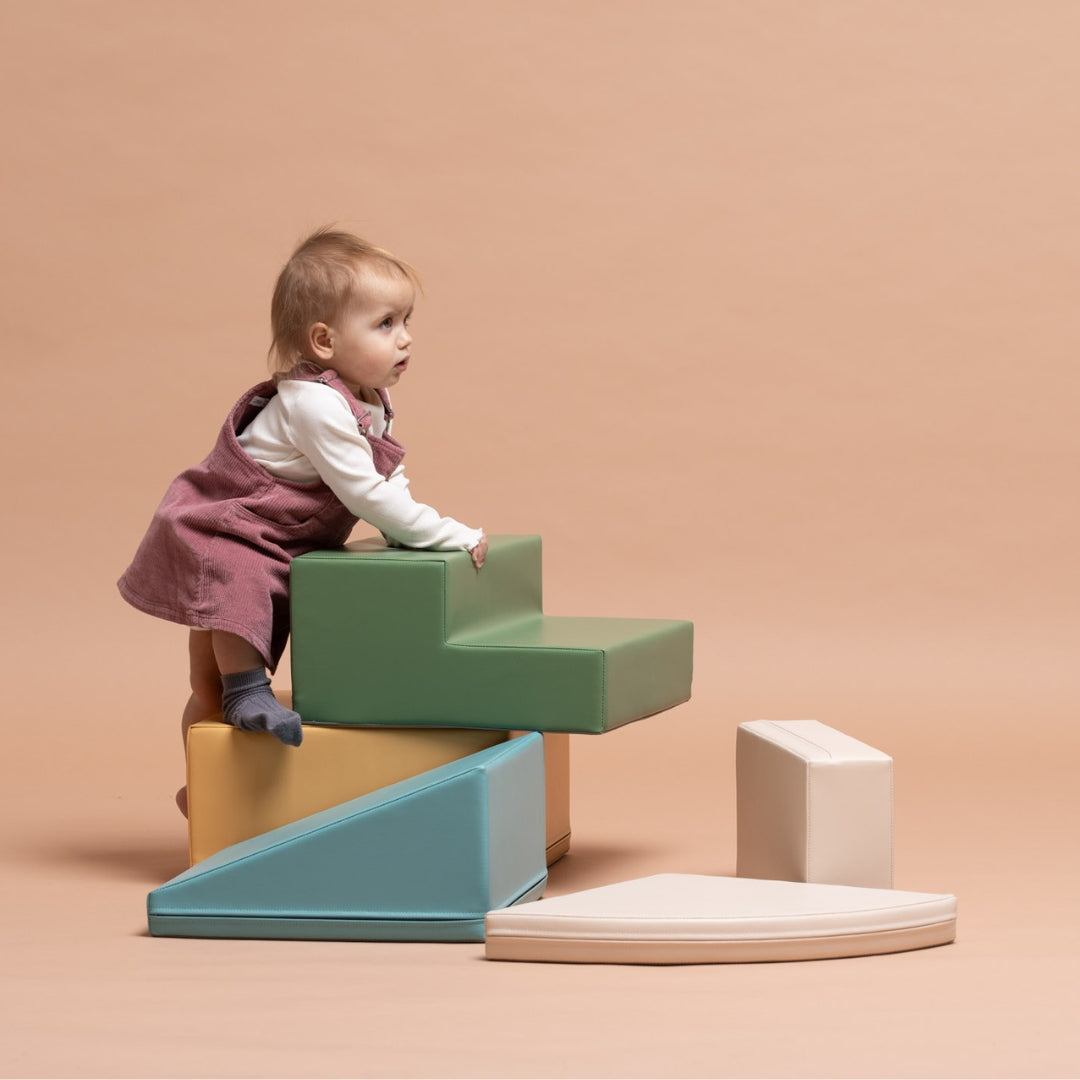 Young toddler crawling and climbing on beige-turquoise foam play blocks designed for motor skill development