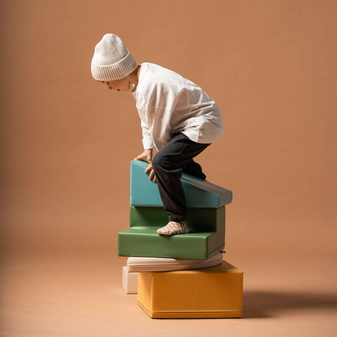 Child balancing and climbing on stackable beige and turquoise soft play blocks in a corner climber set