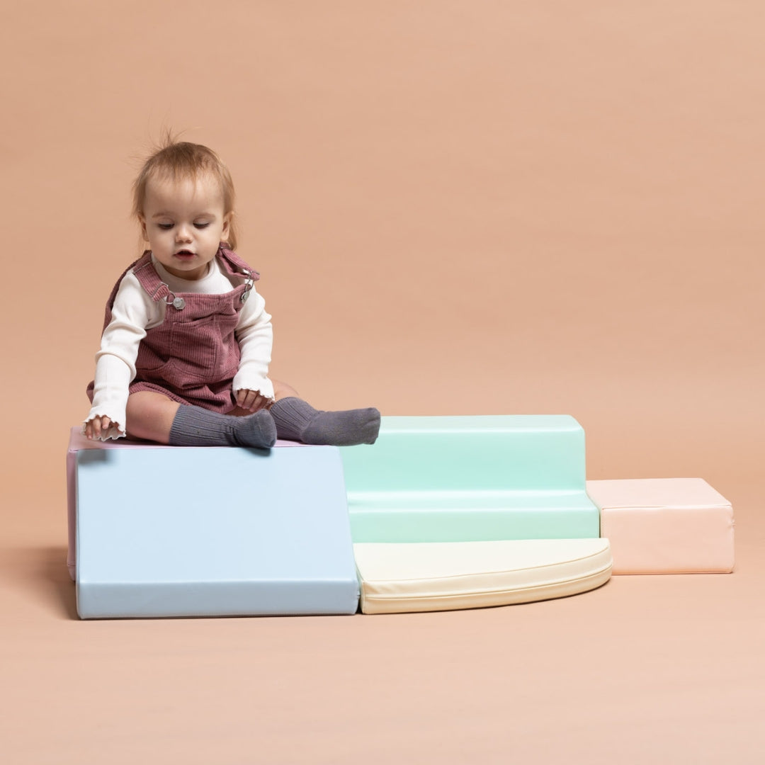 Toddler sitting on pastel soft play foam blocks arranged as a corner climber set