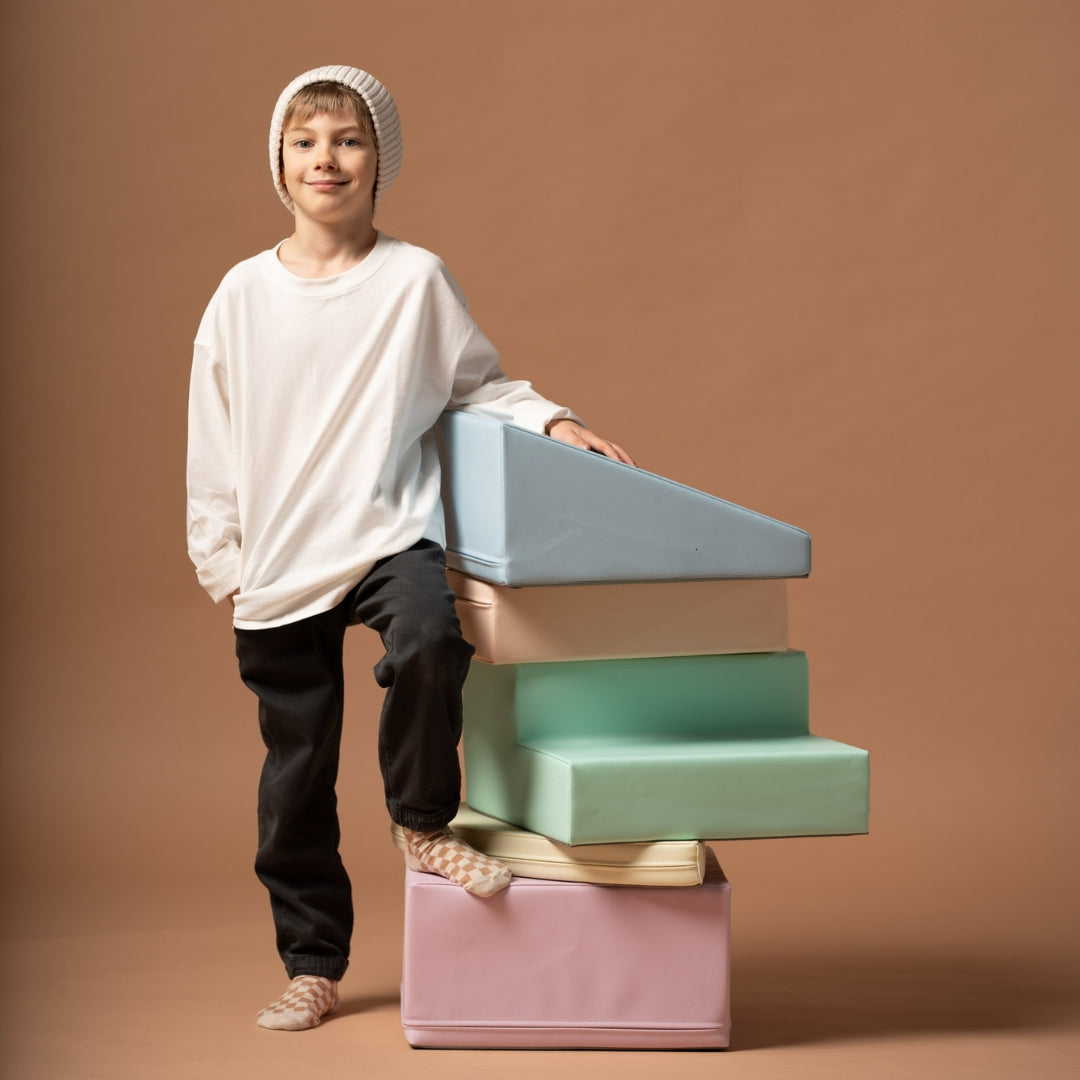 Child standing next to vertical stack of pastel soft play climbing blocks arranged in a tower