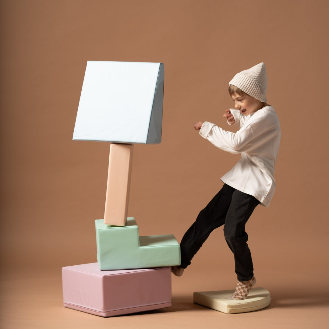 Child playing and balancing with pastel-colored soft foam blocks stacked into a creative tower shape