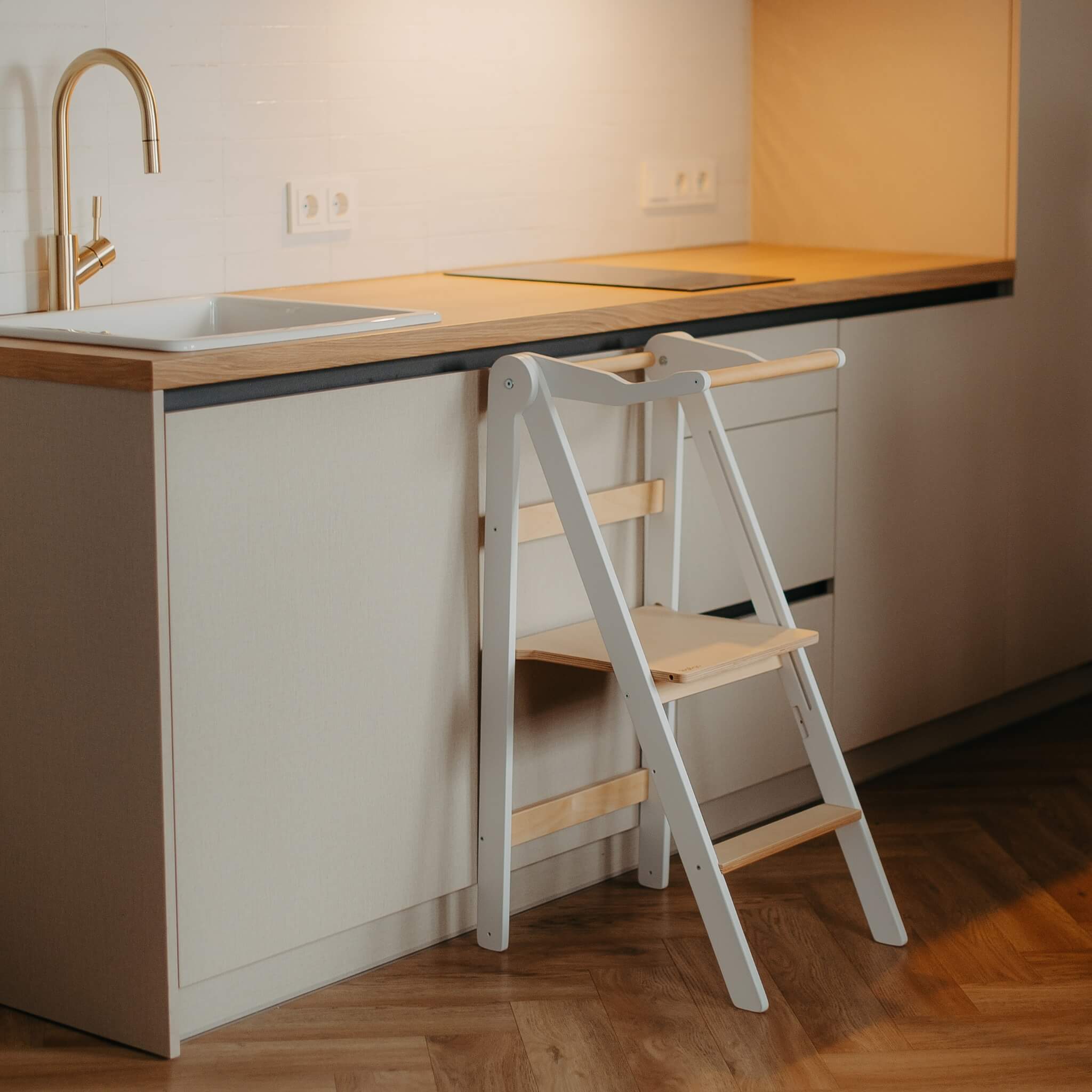 Foldable helper tower stored compactly under kitchen counter showing space-saving design