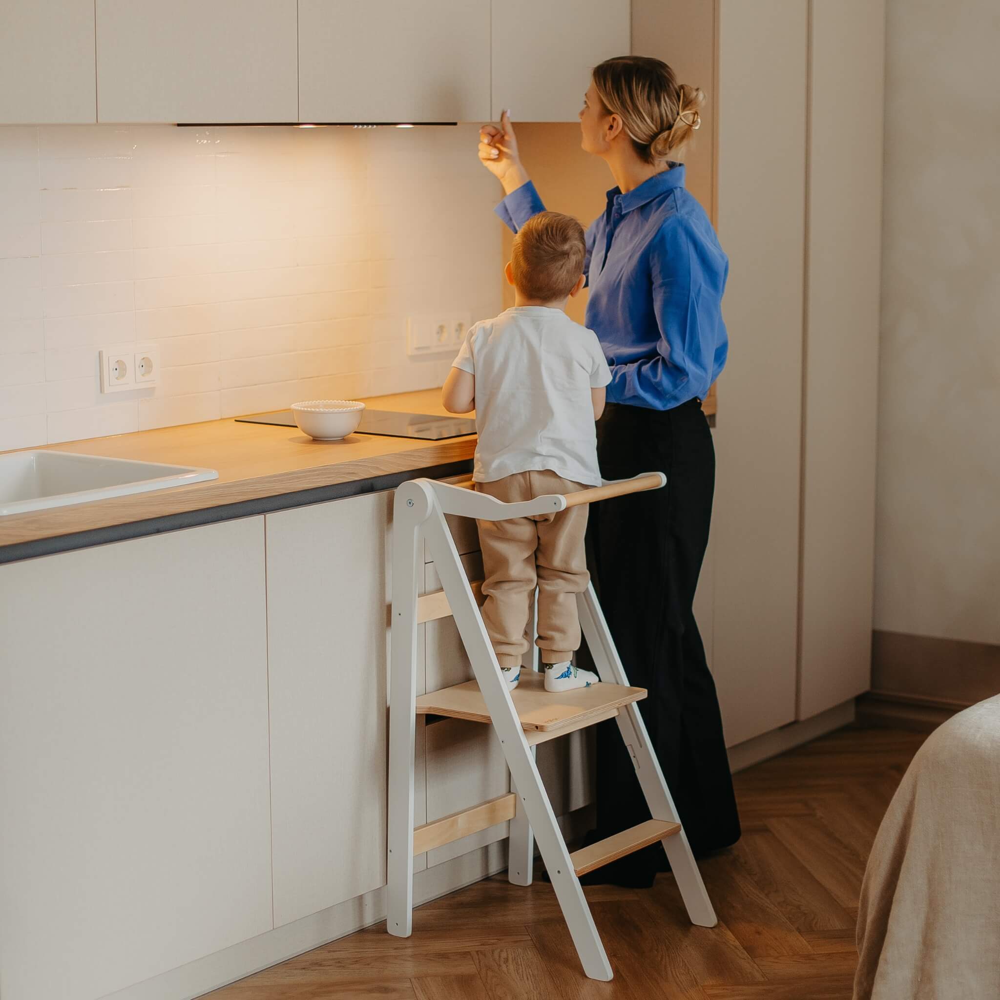 Toddler using foldable learning tower at kitchen counter with safety rail for everyday activities