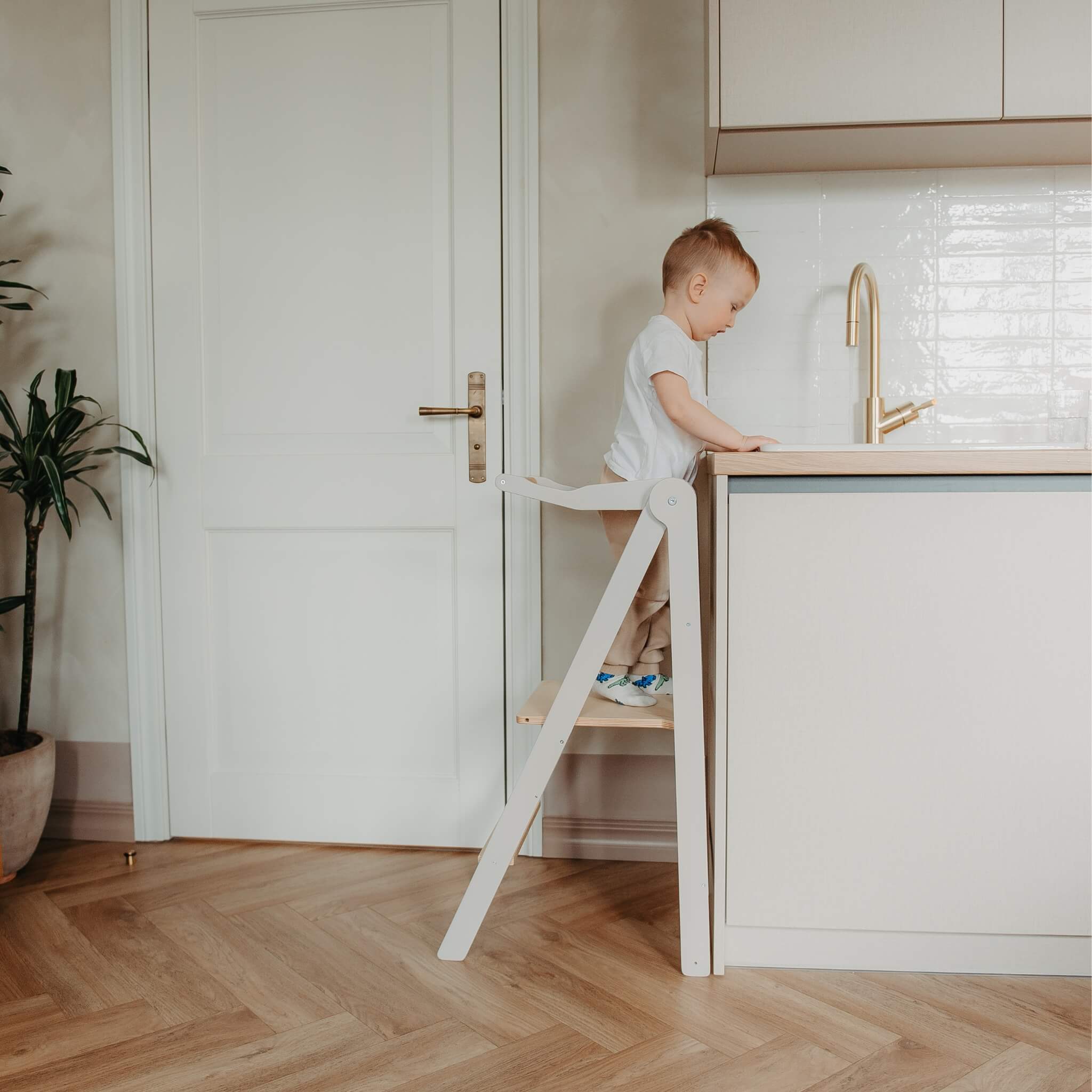 Foldable wooden learning tower in natural color placed in a modern kitchen interior