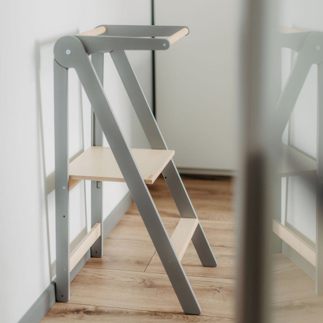 Grey wooden helper tower with a removable rail, designed for safe and versatile use by children