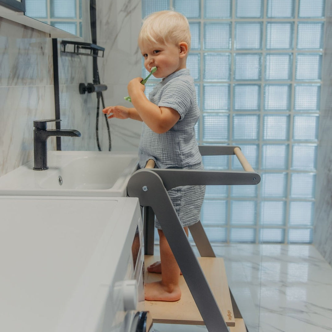Child using a step stool helper tower to reach the sink in a bathroom