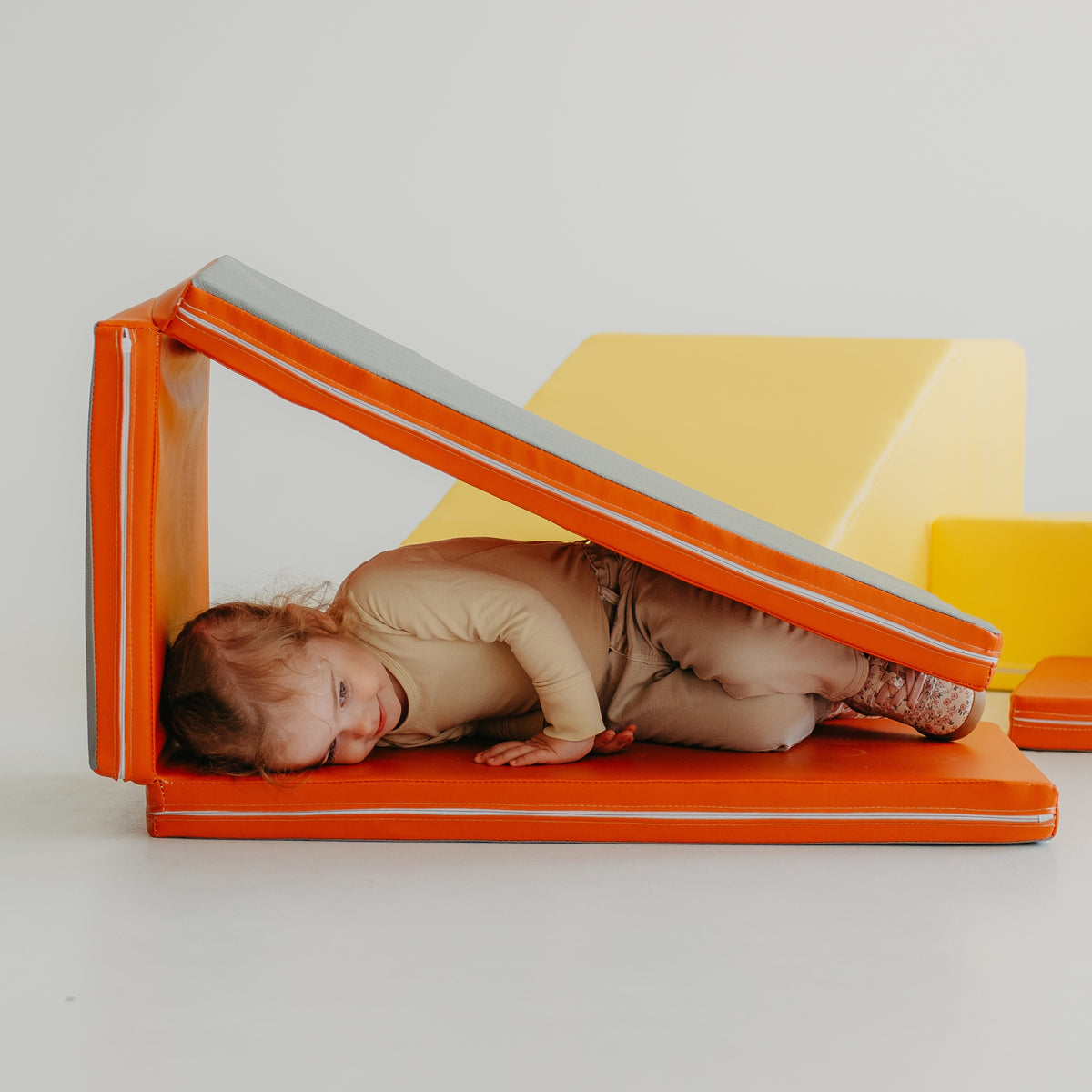 Child lying inside a tunnel built with the orange Kubo Blocks MATO foam play mat