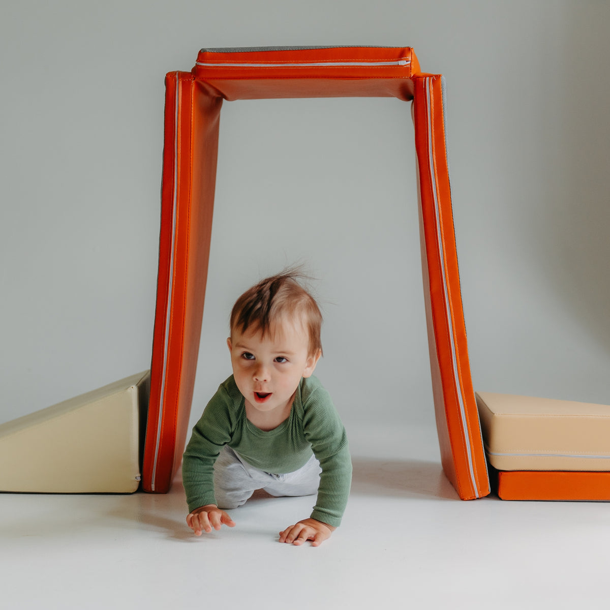 Child crawling through a tunnel made with the orange Kubo Blocks MATO foldable play mat