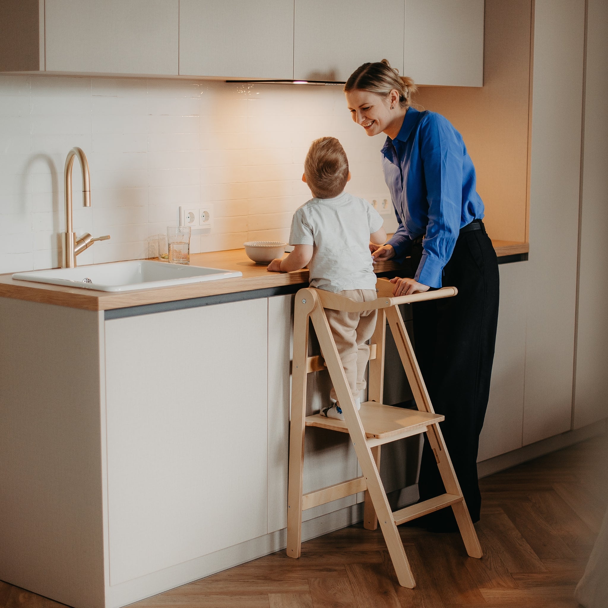 Parent assisting child in foldable helper tower during kitchen activity