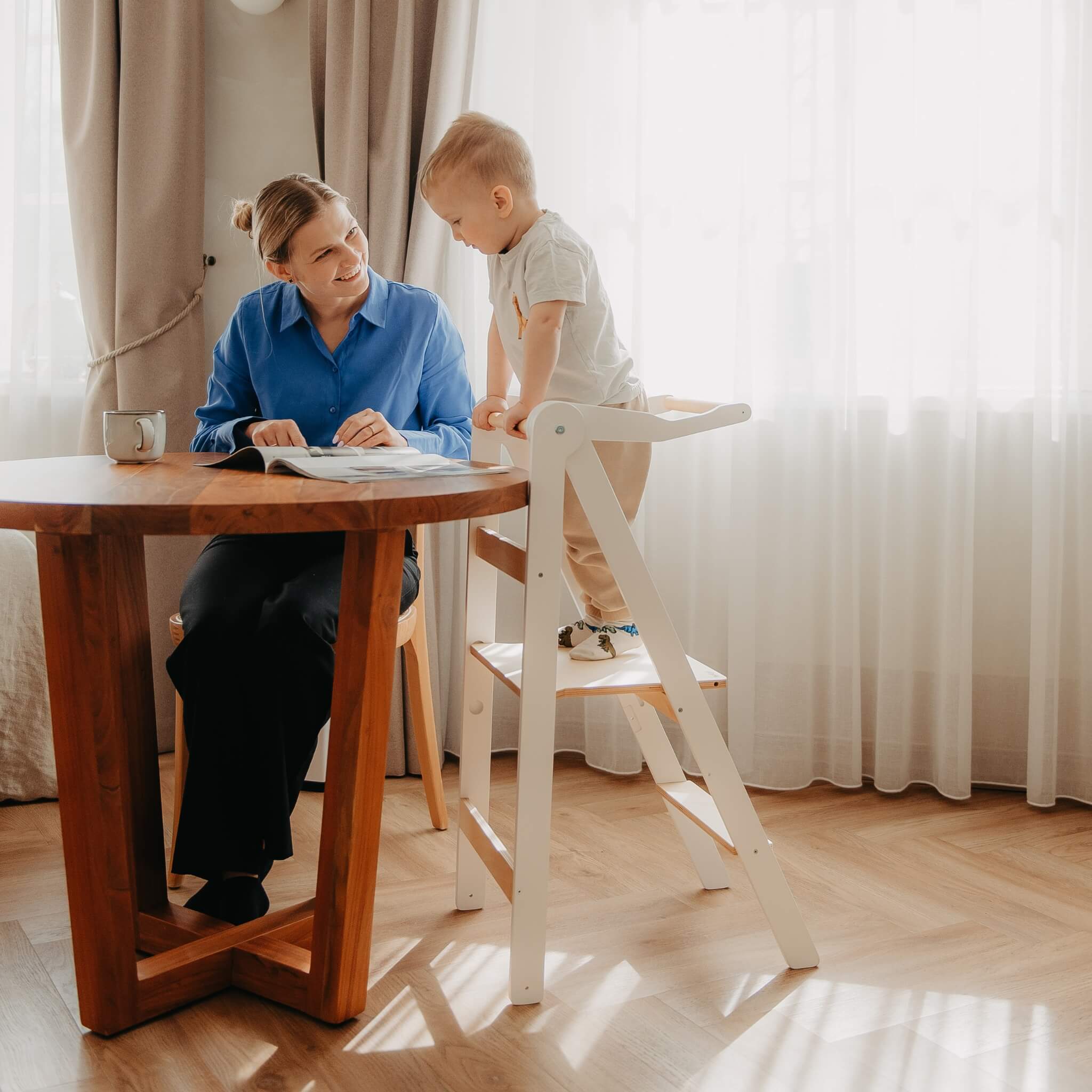 Parent and child interacting while using foldable helper tower in kitchen