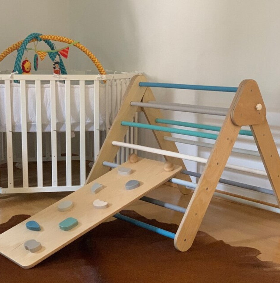 Wooden climbing triangle with matching pastel-colored ramp next to a crib in a room