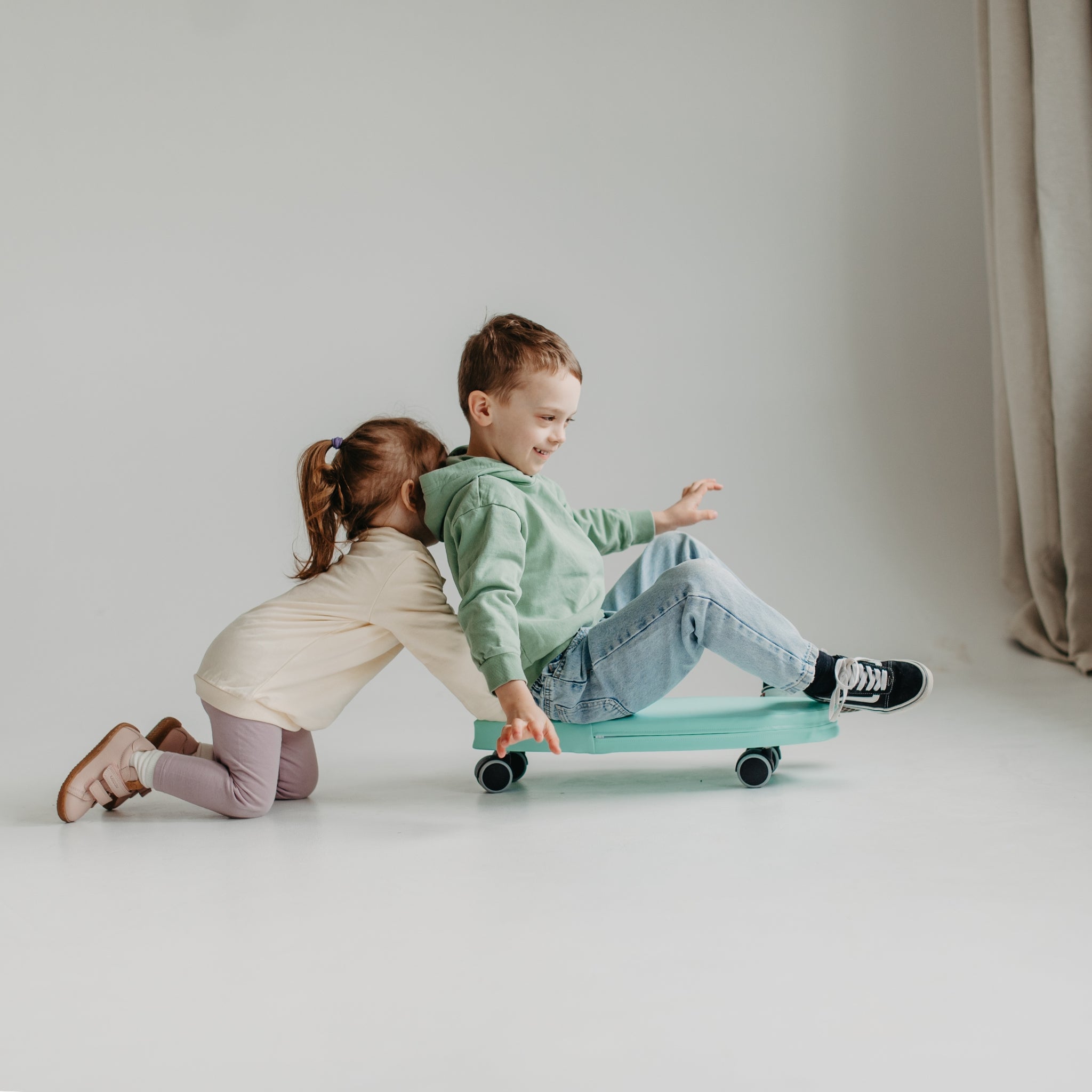 Two children playing with green foam surf ride on toy, indoor movement and balance toy