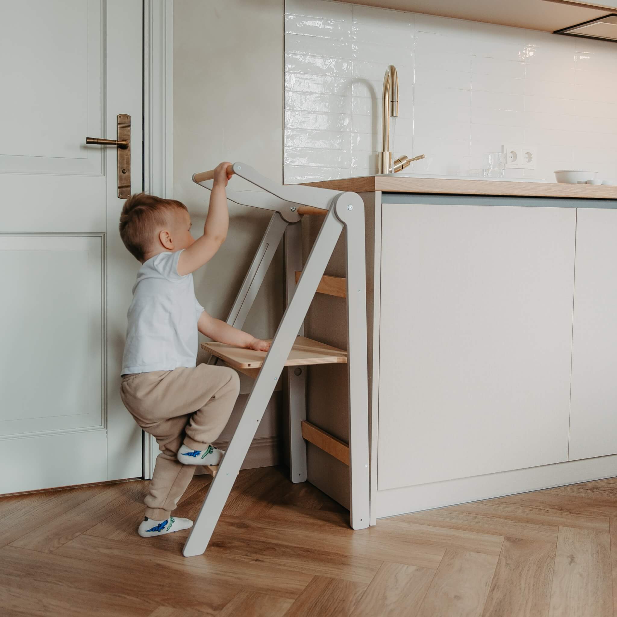 Toddler climbing foldable helper tower to participate in kitchen activities