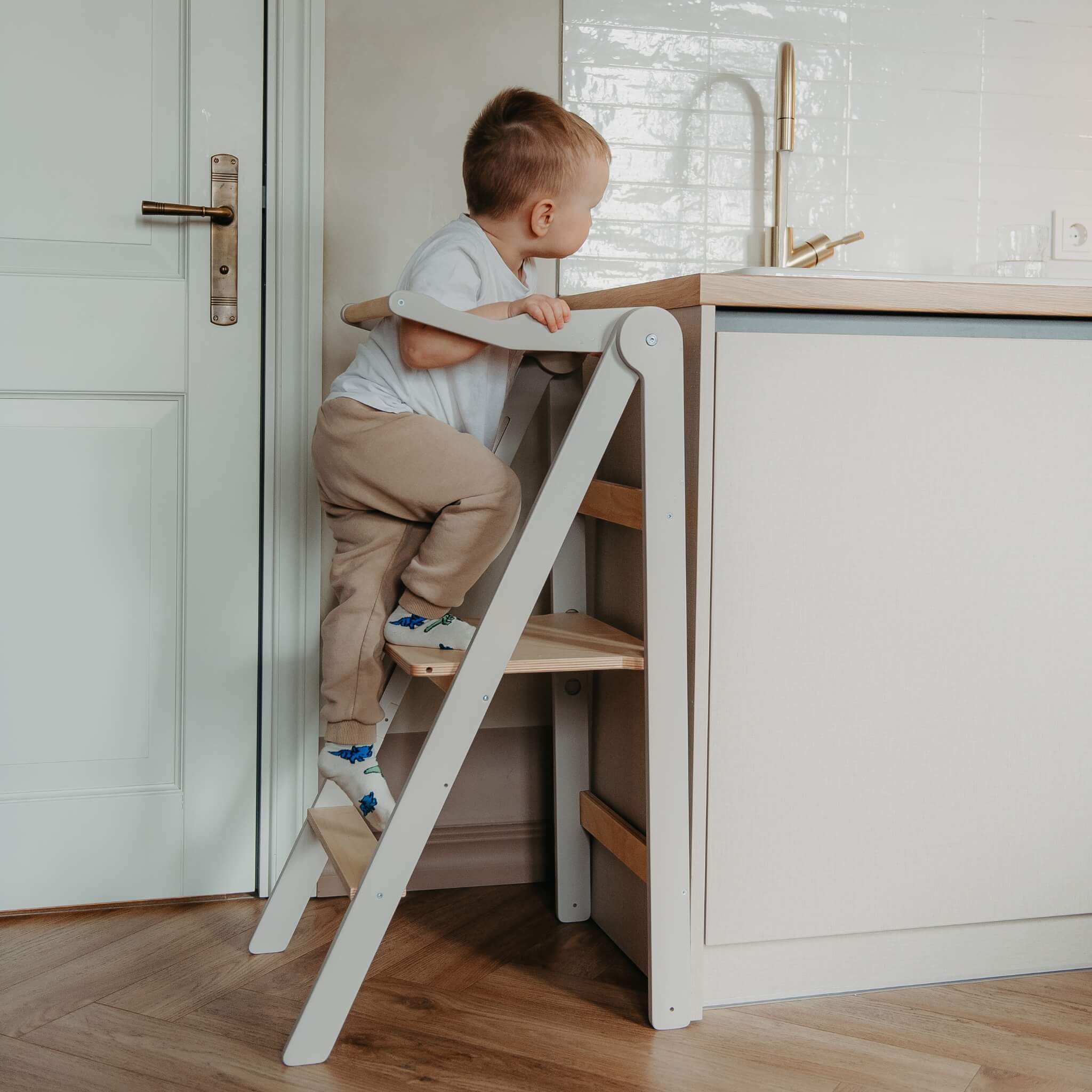 Toddler climbing foldable helper tower to reach kitchen counter safely