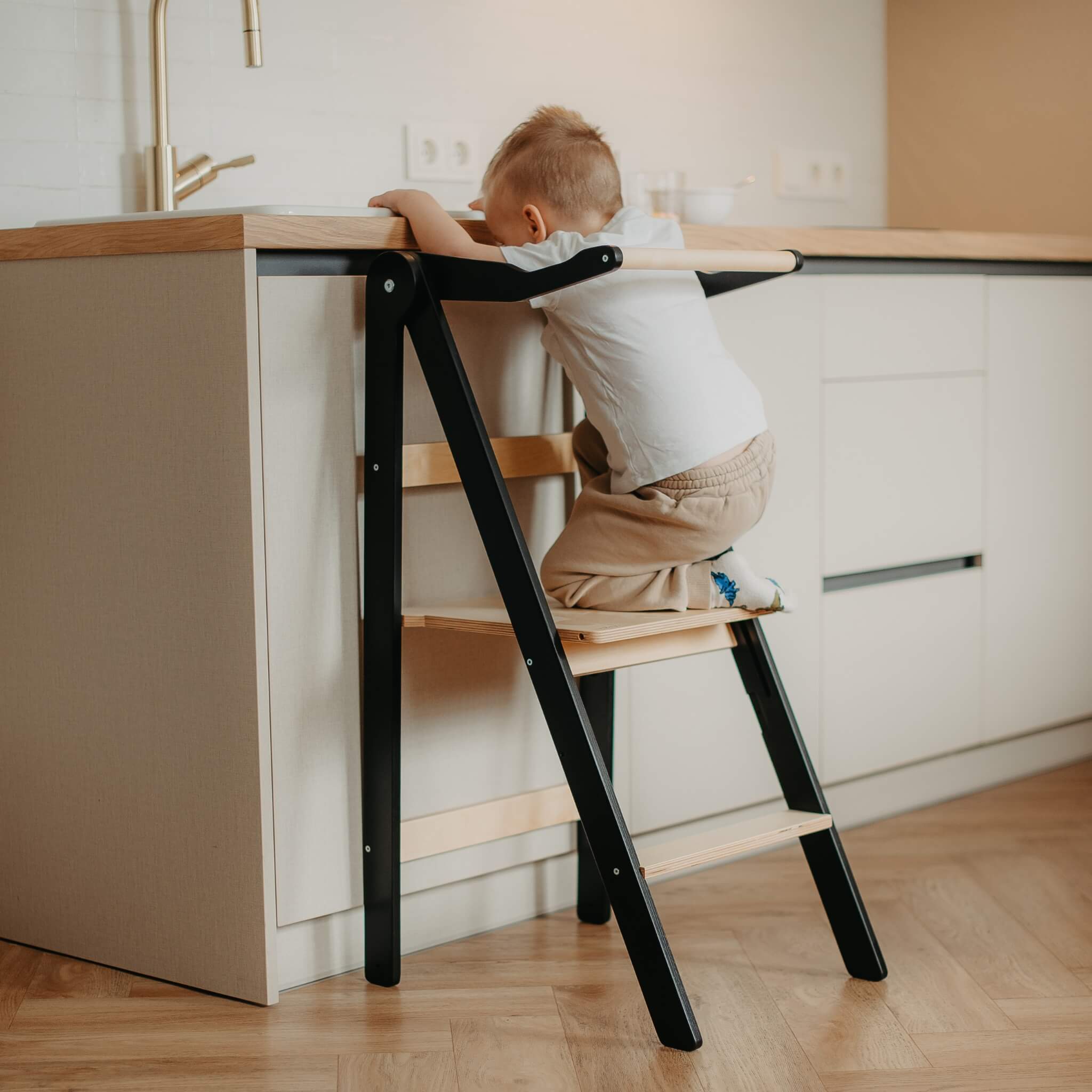 Toddler climbing foldable learning tower with safety rail in modern kitchen setting