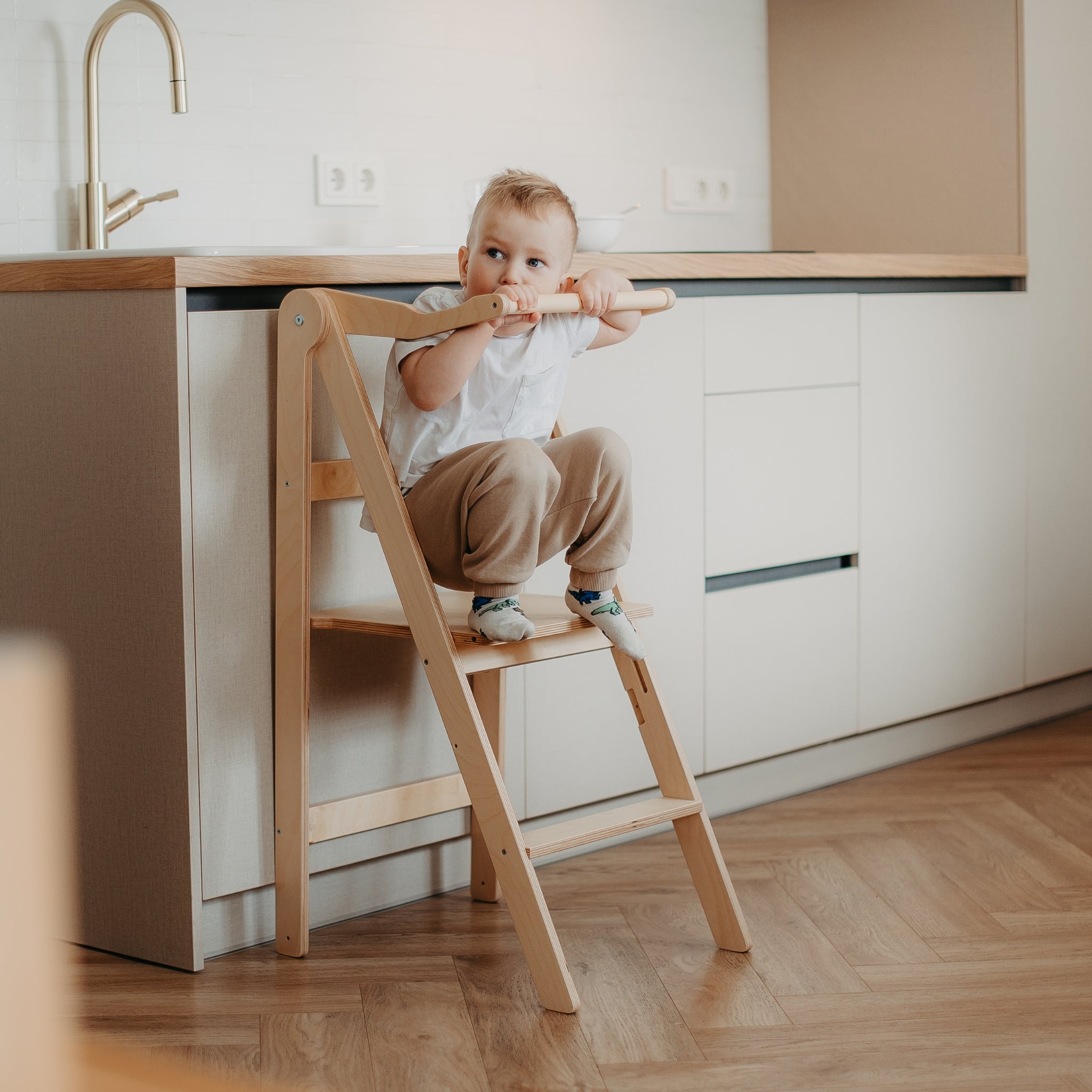 Toddler standing in white foldable learning tower at kitchen counter