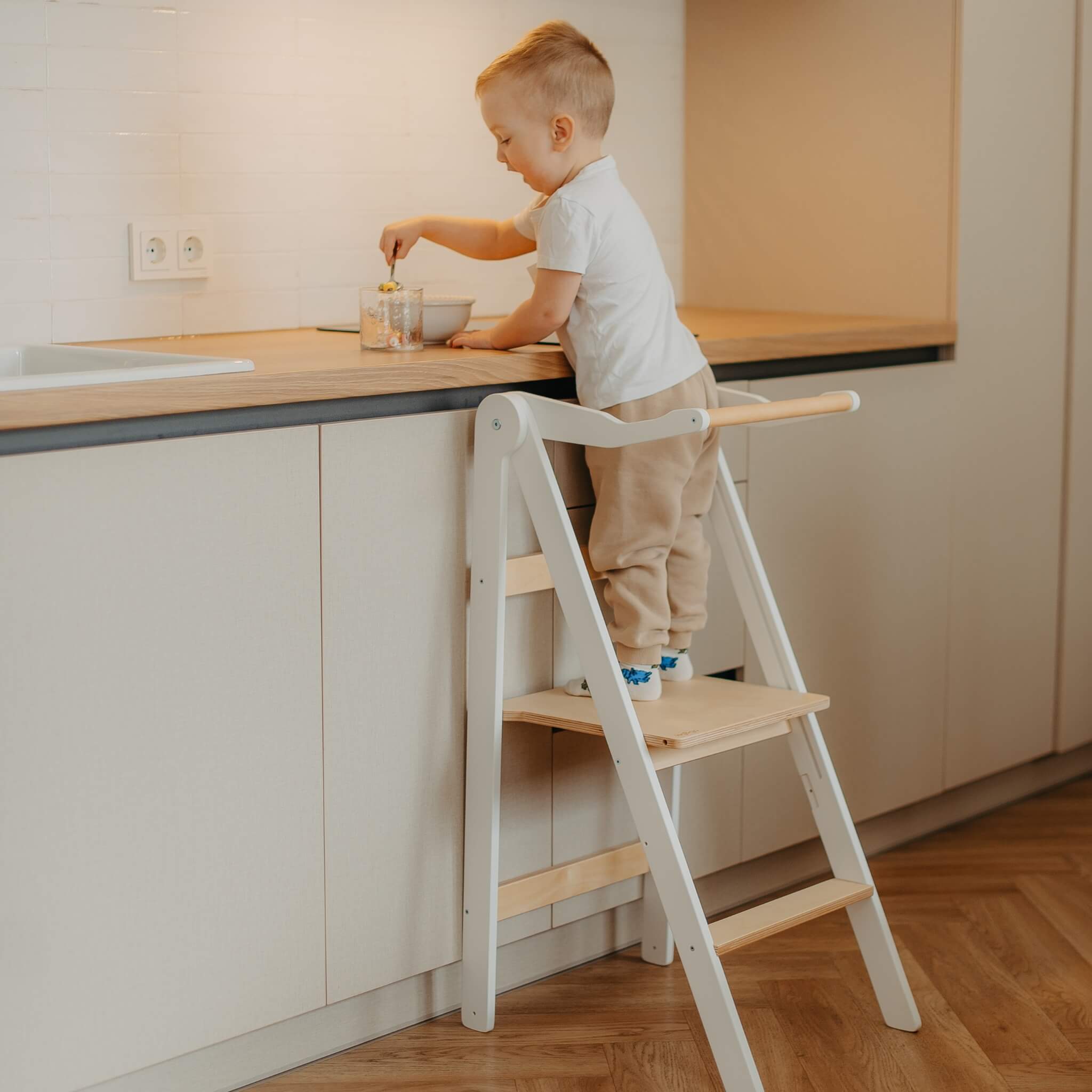 Toddler using wooden learning tower to safely reach kitchen countertop
