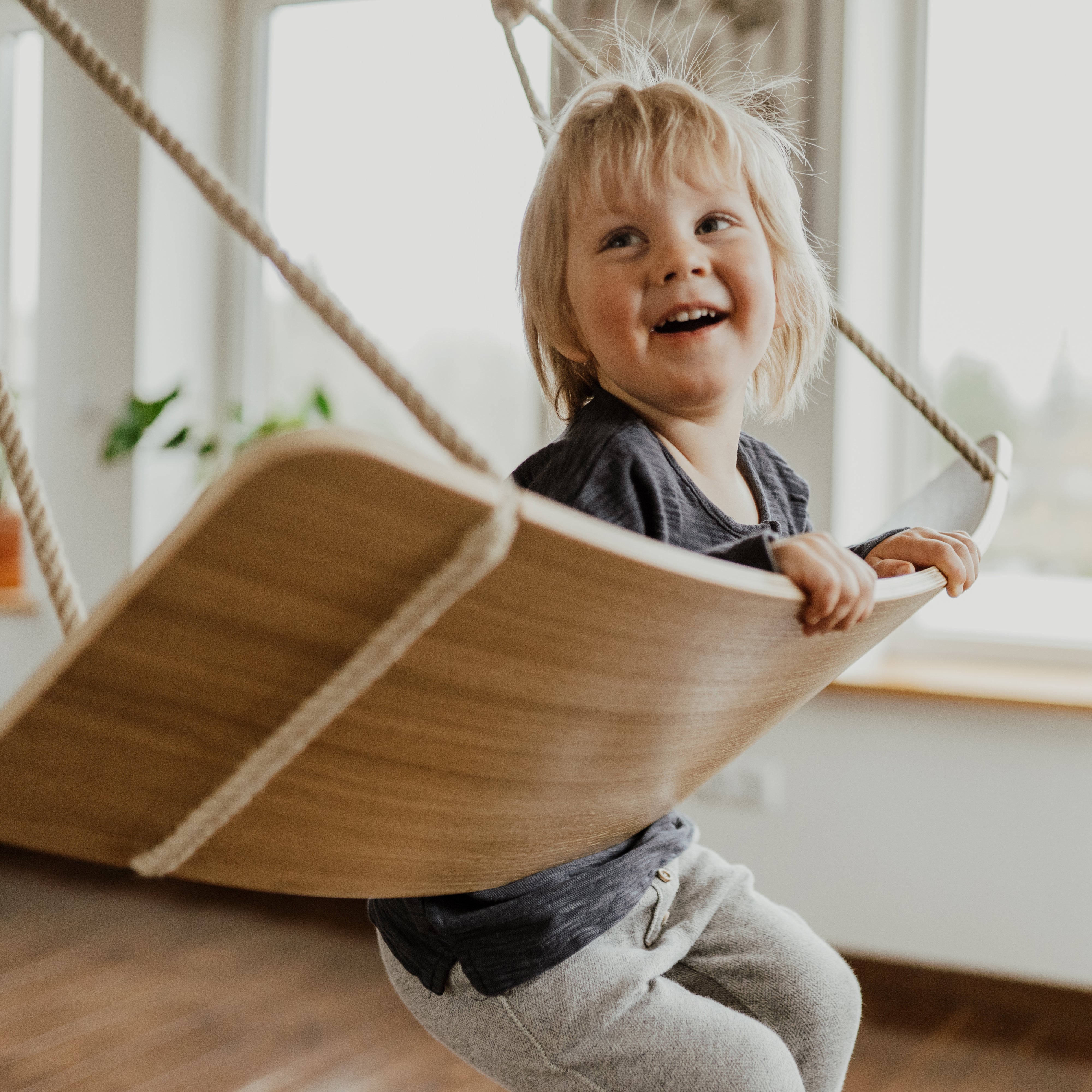 Child playing on wooden balance board swing indoors