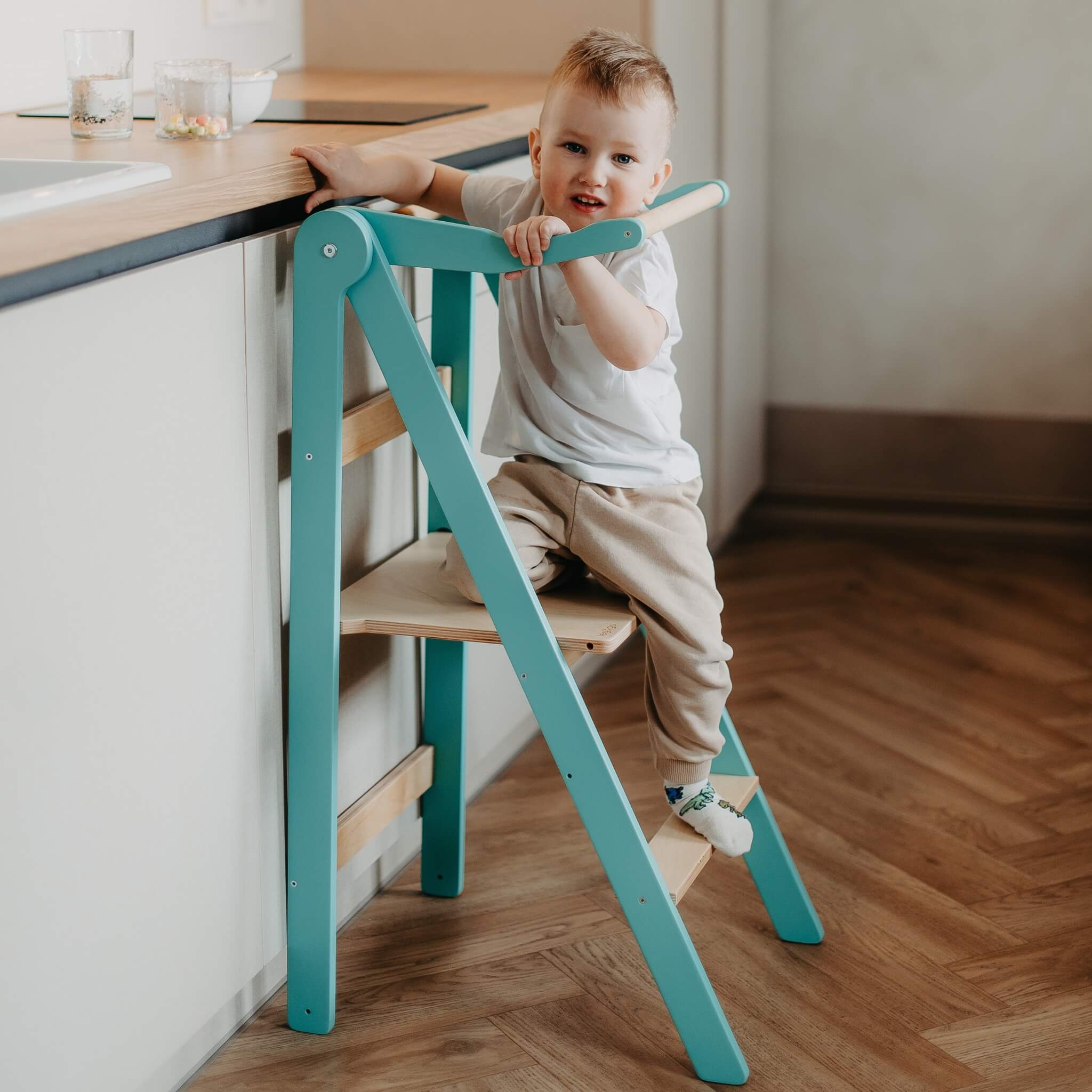 Turquoise foldable learning tower used by toddler as a kitchen helper stool