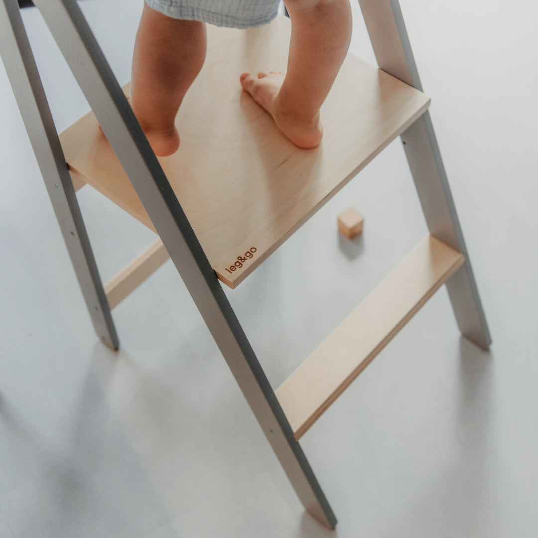 Child standing barefoot on a grey leg&go kitchen tower, exploring safely and engaging in imaginative play in the kitchen